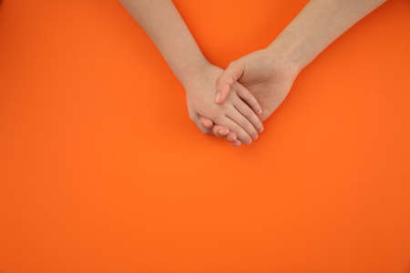 Mother holding hands with her child on orange background, top view. happy familyの写真素材