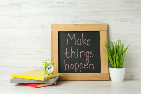 Small chalkboard with motivational quote Make Things Happen, notebooks, alarm clock and plant on white wooden tableの写真素材