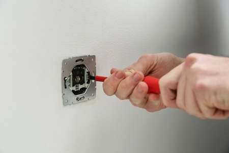 Electrician with screwdriver repairing power socket, closeup