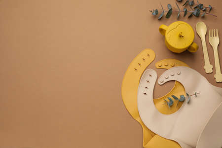 Flat lay composition with baby feeding accessories and bibs on brown background, space for textの写真素材