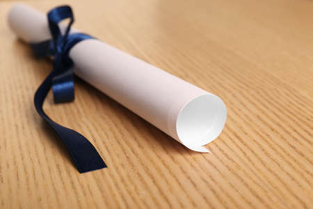 Graduation diploma tied with blue ribbon on wooden table, closeupの写真素材