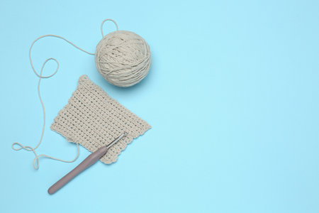 Clew of thread, knitting and crochet hook on light blue background, flat lay. Space for text