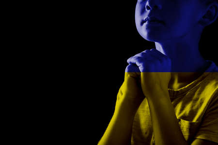 Pray for Ukraine. Double exposure of little boy praying on black background and Ukrainian national flagの写真素材