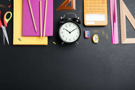 Flat lay composition with alarm clock and different stationery on blackboard, space for text. school timeの写真素材