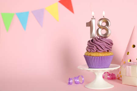 Delicious cupcake with number shaped candles on pink background, space for text. Coming of age party - 18th birthdayの写真素材
