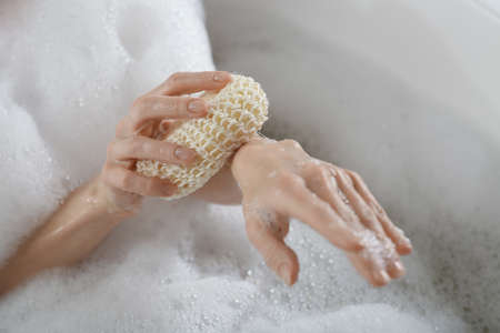 Woman rubbing her forearm with sponge while taking bath, closeupの写真素材