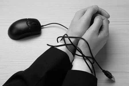 Closeup view of woman with her hands tangled in cable of computer mouse at wooden table, black and white effect. internet addictionの写真素材
