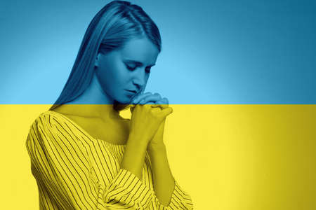 Pray for Ukraine. Double exposure of young woman praying and Ukrainian national flagの写真素材
