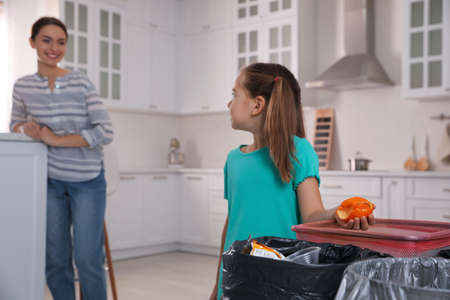 Little girl throwing tangerine peel into trash bin in kitchen. Separate waste collectionの写真素材