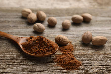 Spoon with nutmeg powder and seeds on wooden table, space for textの写真素材