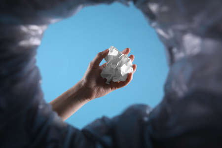 Bottom view of woman throwing crumpled paper into trash bin on light blue background, closeupの写真素材