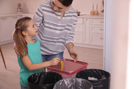 Young woman and her daughter throwing banana peel into trash bin in kitchen. Separate waste collectionの写真素材