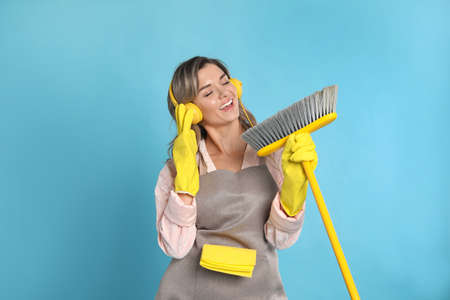Beautiful young woman with headphones and floor brush singing on light blue backgroundの写真素材