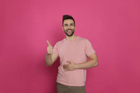 Happy man touching his belly and showing thumb up on pink background. concept of healthy stomachの写真素材