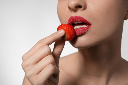 Young woman with lips covered in sugar holding strawberry on light background, closeupの写真素材