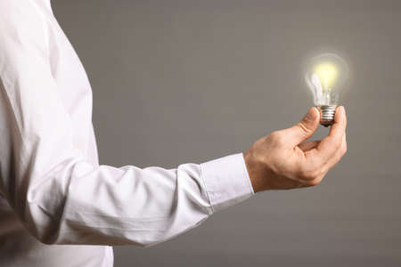 Glow up your ideas. Close up view of man holding light bulb on gray backgroundの写真素材