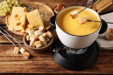 Dipping pieces of bread into tasty cheese fondue on wooden tableの写真素材