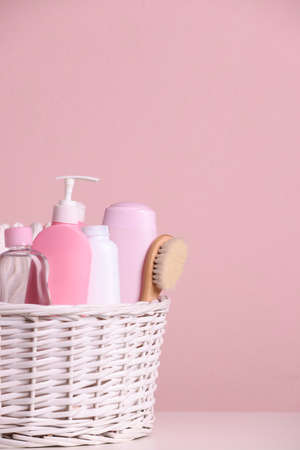 Wicker basket with baby cosmetic products and bath accessories on white table against pink background. Space for textの写真素材