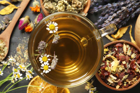 Glass cup of aromatic freshly brewed tea near different dry herbs on black table, flat layの写真素材