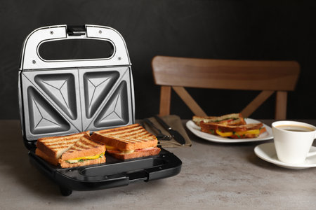 Modern grill maker with tasty sandwiches and cup of coffee on light gray table