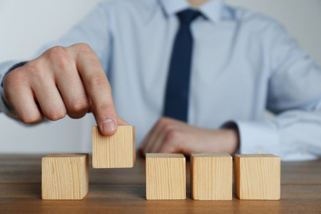 Businessman arranging blank cubes on wooden table, closeup. Space for textの写真素材