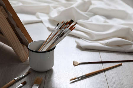 Different brushes near stand with canvas on floor in artist's studio, space for textの写真素材