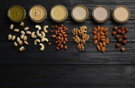 Jars with butters made of different nuts and ingredients on black wooden table, flat lay. Space for...