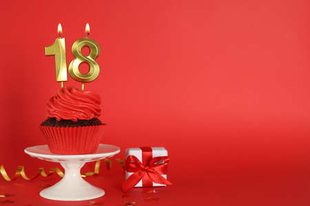 Delicious cupcake with number shaped candles on red background, space for text. Coming of age party - 18th birthdayの写真素材