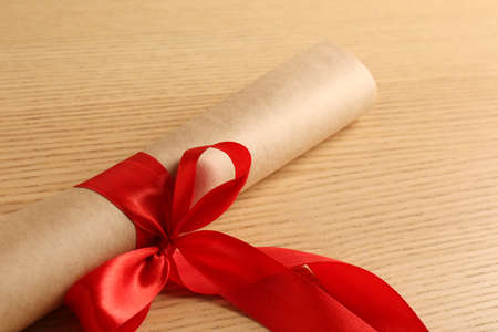 Graduation diploma tied with red ribbon on wooden table, closeupの写真素材