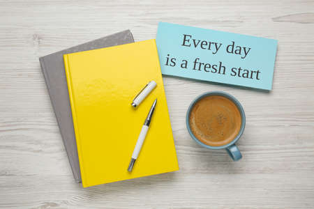 Books, cup of aromatic coffee and card with motivational quote Every Day Is A Fresh Start on white wooden table, flat layの写真素材