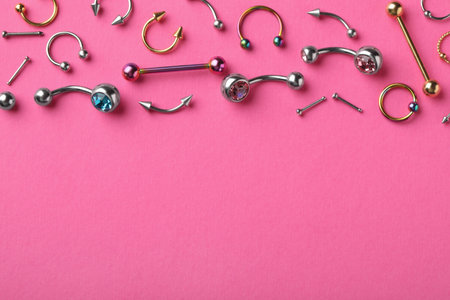 Stylish piercing jewelry on pink background, flat lay. Space for textの写真素材