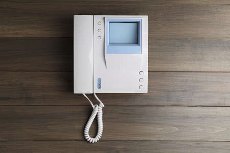 Modern intercom system with handset on wooden background, top view