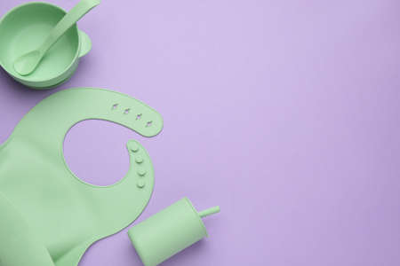 Flat lay composition with baby feeding accessories and bib on violet background, space for text