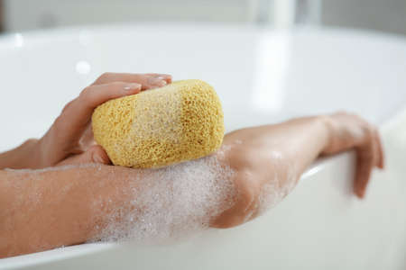 Woman with sponge taking bubble bath, closeup