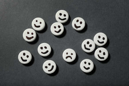Pill with sad face among happy ones on black background, flat lay. depression conceptの写真素材