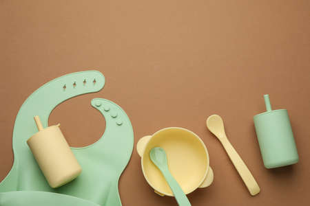 Flat lay composition with baby feeding accessories and bib on brown background, space for text
