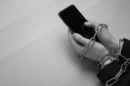 Above view of internet addicted woman with chained hands using smartphone at wooden table, space for text. black and white effectの写真素材