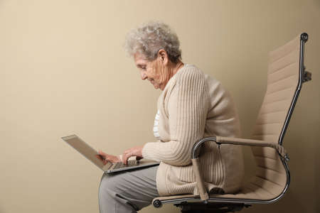 Elderly woman with poor posture using laptop on beige backgroundの写真素材
