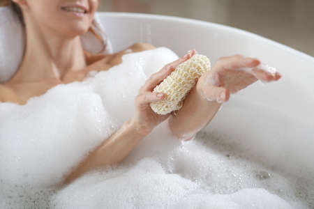 Woman rubbing her forearm with sponge while taking bath, closeup
