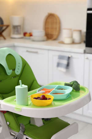High chair with food in baby tableware on tray indoorsの写真素材