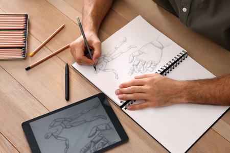Man drawing in sketchbook with pencil at wooden table, closeupの写真素材