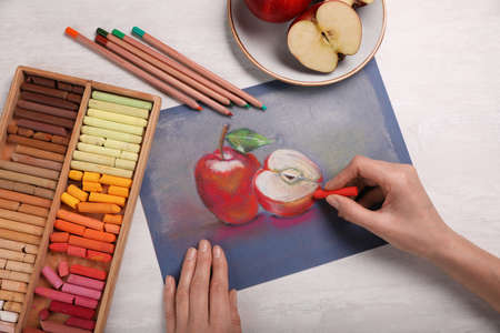 Woman drawing apples on paper with soft pastels at white table, top viewの写真素材