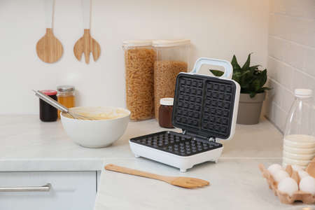 Modern electric waffle maker and ingredients on white countertop indoorsの写真素材