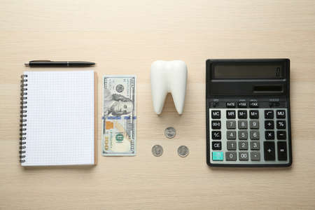 Flat lay composition with ceramic model of tooth and money on wooden table. Expensive treatmentの写真素材