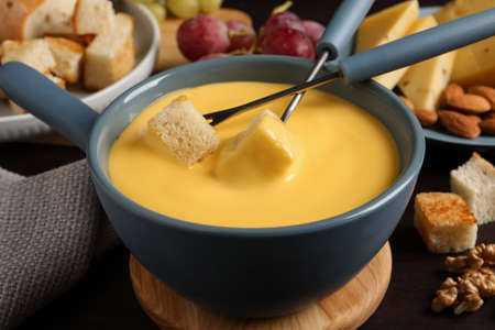 Pot of tasty cheese fondue and forks with bread pieces on wooden table, closeupの写真素材