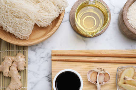 Flat lay composition with uncooked rice noodles, soy sauce and chopsticks on white marble tableの写真素材