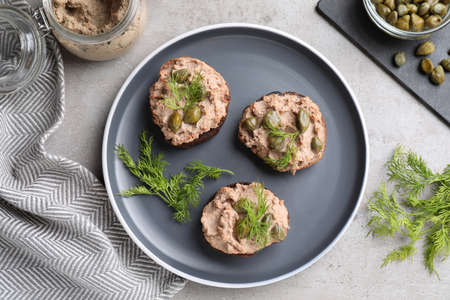 Slices of bread with delicious pate, capers and dill on light gray table, flat lay