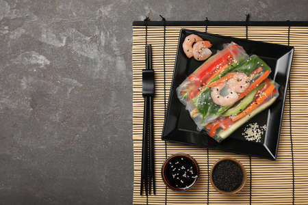Delicious rolls wrapped in rice paper served on gray table, top view. Space for text