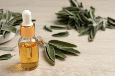 Bottle of essential sage oil, plant twigs and leaves on wooden table. Space for textの写真素材