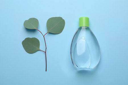 Bottle of baby oil and eucalyptus leaves on light blue background, flat layの写真素材